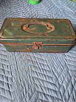 Closed green metal toolbox showing rust and size reference