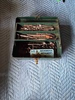 Closed-in view of open green metal toolbox showing trays filled with assorted drill bits and tin labelled "Mathematical Instruments"