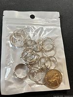 Bag containing multiple silver-tone rings alongside a quarter