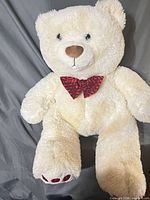 Front view of cream teddy bear with red bowtie and paw pad detail