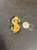 front view of gold-tone $ money clip beside coin for scale