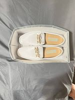 Top view of both loafers in box showing white uppers, gold-tone bit, size and insole