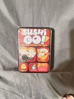 Front of sealed Sushi Go! tin showing title, player count, age range