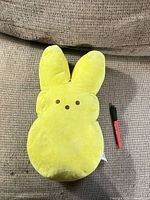 Front view of yellow Peeps bunny plush beside pen for size reference