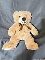 front view of beige plush teddy bear with brown ribbon