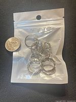 Bag containing silver-tone rings beside a coin for scale