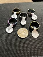 Five stainless steel band rings around a coin showing finishes and size tags
