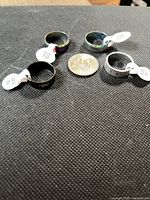 Four stainless steel band rings with size tags and a coin for scale