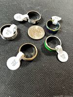 Five stainless steel rings with size tags and quarter for scale