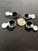 All four stainless steel rings with size tags around coin for scale