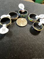 Group of seven stainless steel rings with size tags and a coin for scale