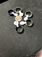 Six stainless steel rings around a quarter showing size tags
