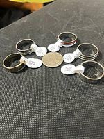 Five stainless steel rings with size tags arranged around coin