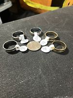 Six rings of differing finishes arranged around a coin for scale