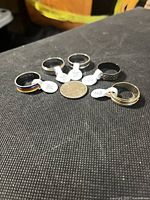 Six stainless steel size 11 rings arranged around a coin showing different finishes