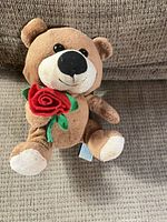 Front view of brown plush teddy bear holding red felt rose