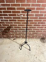 Full view of wrought iron floor candlestand against brick wall