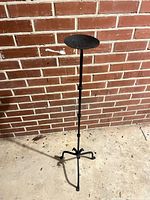Full view of wrought iron floor candlestand against brick wall