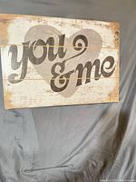 Front of wooden sign showing “you & me” text and heart design