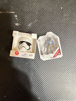 Mini Stormtrooper helmet box and Mandalorian figure blister pack on textured surface