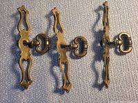 Three brass-finish ornate drawer pulls laid out front view