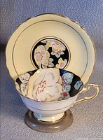 Cup nested in saucer showing Hibiscus pattern, cream exterior, gold trim