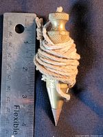Full plumb bob beside ruler showing size and cotton line