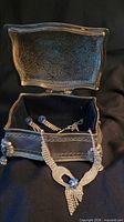 Open silver-plated jewelry box with necklace draped and earrings inside