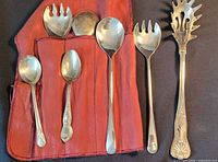 All seven silver-plated utensils displayed with red fabric roll