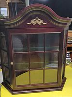 Front view of wood wall cabinet showing glass-paned door and gold embellishment