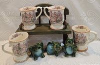 Four rabbit-themed mugs on wooden stand with three frog figurines below