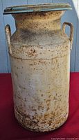 Full view of steel milk can on red cloth