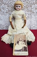 Full view of bisque doll seated with photograph in front