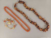 All three jewellery pieces laid out: tiger's eye necklace, orange bead necklace, gold-filled bracelet