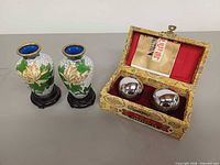 Two cloisonné vases on stands beside brocade box containing pair of chrome Baoding balls