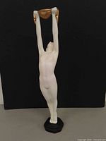 Front view of white nude female candle holder with gold cloth raised overhead on black base