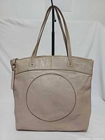 Front view of Coach gray leather tote showing embossed circular logo patch and straps