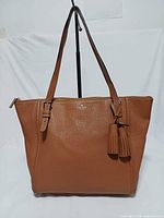 Front view of brown Kate Spade tote with tassels visible