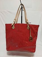 Front view of red patent leather Michael Kors Jet Set tote with straps and MK charm visible