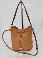 Front view showing suede material, drawstring closure, logo plaque, and full strap