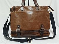 Front view showing flap, buckle straps, handles, crossbody strap