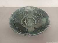 Top view of shallow green glazed pottery bowl showing spiral well and rim notches