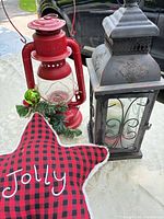 Overall view of red kerosene lantern, black lantern, plaid star pillow on table
