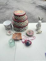 Full lot view including tins, figurine, heart ornament, wooden coasters, glass jar, cork coasters, paperweight, planter, carrot accent