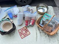 Overall lot showing disposable cups, plates, bowls in zipper bags, wicker baskets, metal bowl, trivet