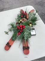 Front view of crossed wooden skis with greenery, berries, ornaments and battery pack