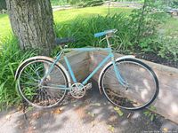 Full view of bicycle leaning against wooden planter, showing frame color, wheel size and fenders
