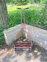 Front full view of red manual reel mower leaning on timber