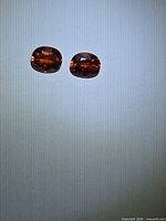 Two burnt orange spessartite garnets on bluish background