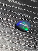 Pear-shaped opal cabochon on textured surface displaying green, red and blue flashes